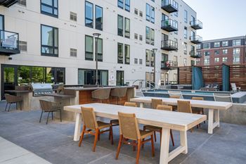 An outdoor patio with tables and chairs and a pool in front of an apartment building